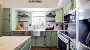 A kitchen with green cabinets, a wooden countertop, stainless steel appliances, and a window with plants on the sill. - Historic Colonial Retreat in Downtown Brunswick (Brunswick)
