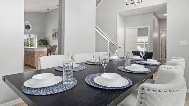 Een eethoek met een donker houten tafel voor vier personen, witte stoelen en een kroonluchter.
