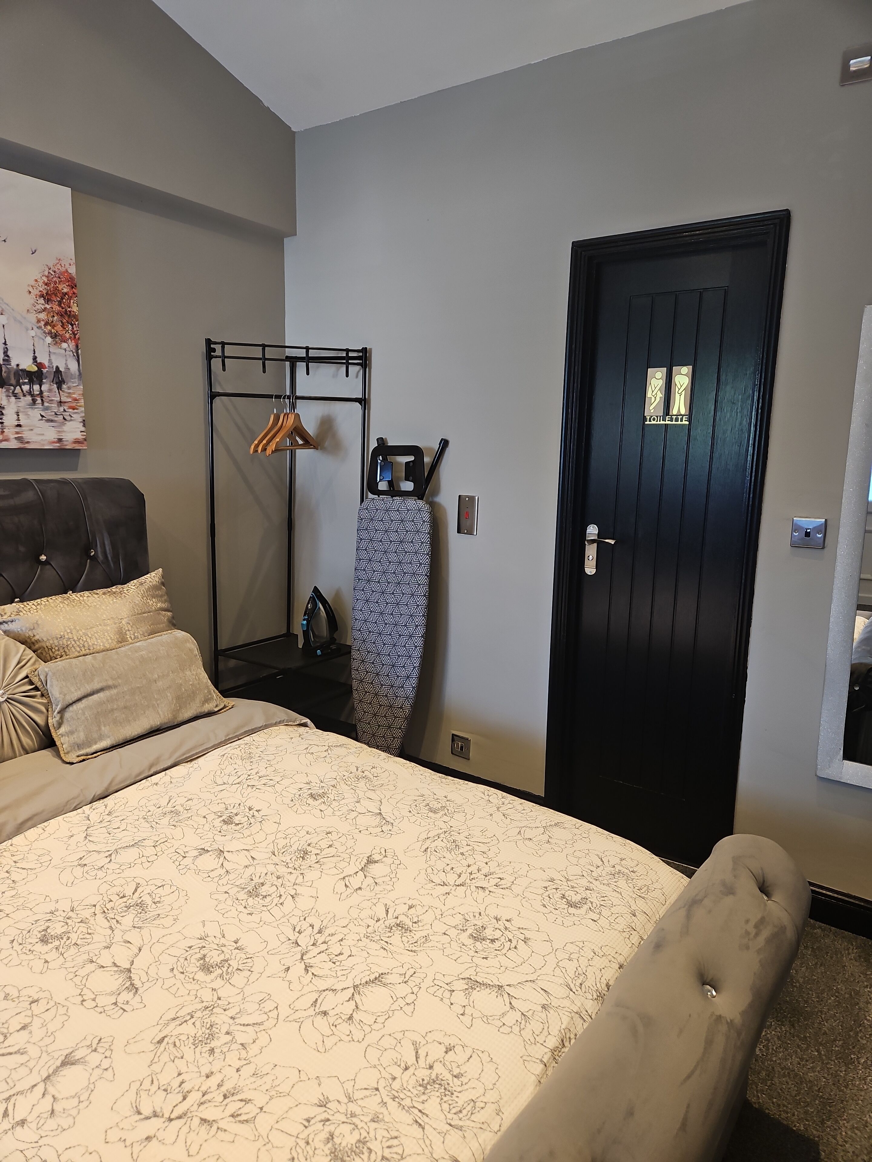 A bedroom with a bed, a wardrobe, a door, and a wall-mounted mirror.