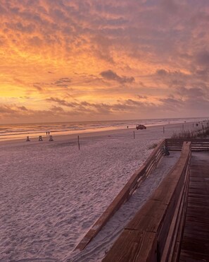 A beach with a wooden boardwalk, sandy beach, and a sunset sky. - Walk to the beach and Flagler Ave-2 bedroom cottage (New Smyrna Beach)