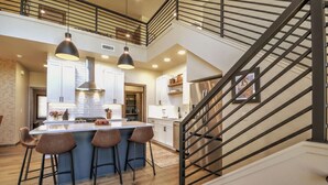 A modern kitchen with a central island, bar stools, pendant lighting, and a staircase with a metal railing. - Private sauna, close to ski mountain and downtown (Red Lodge)
