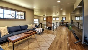 A spacious living area with a dark blue sofa, a wooden coffee table, and a patterned rug. There is a staircase leading to an upper level with a railing. - Private sauna, close to ski mountain and downtown (Red Lodge)