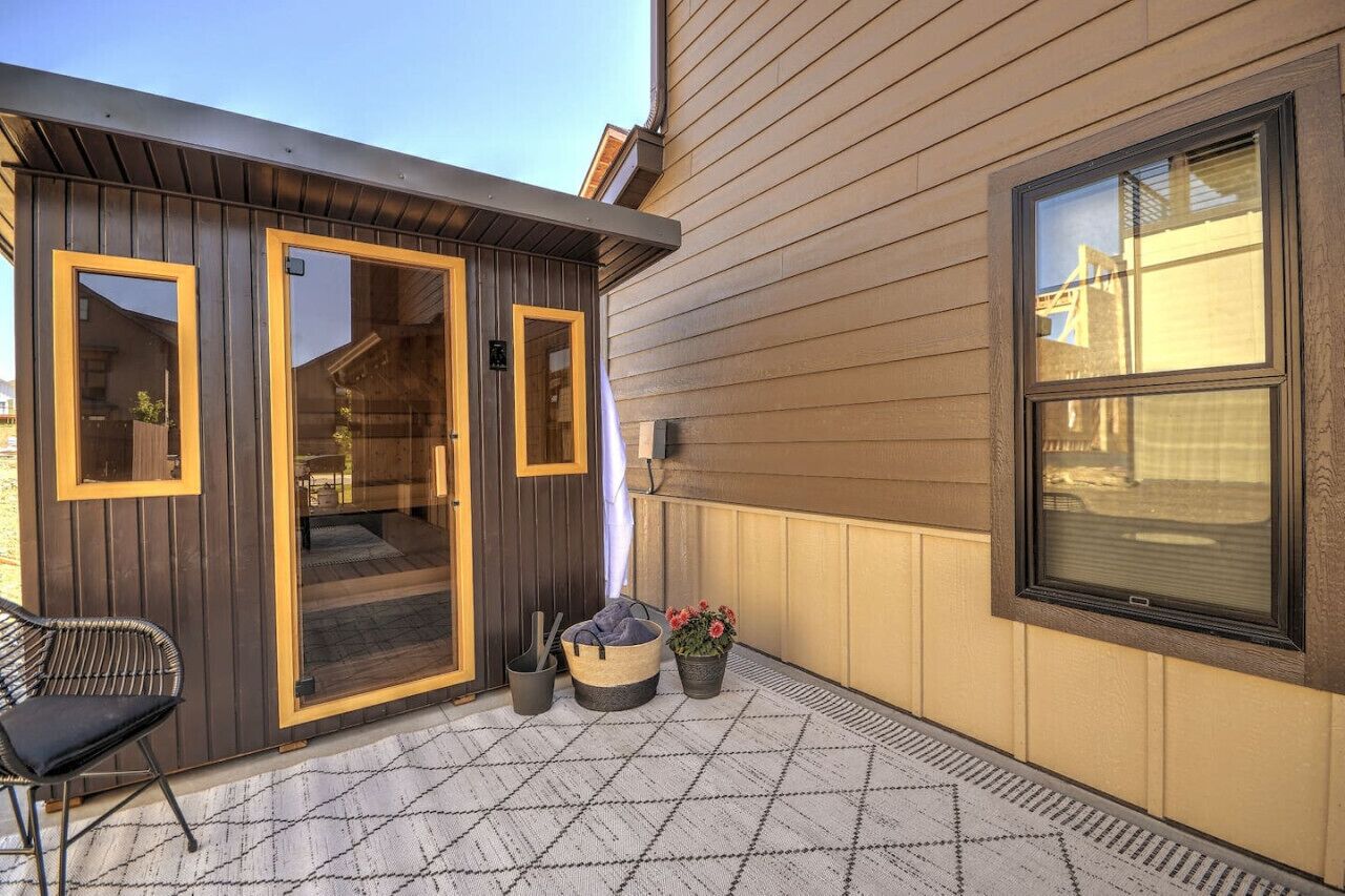 Fachada moderna con puerta y ventana de madera, una silla negra, una cesta tejida y una planta en maceta.
