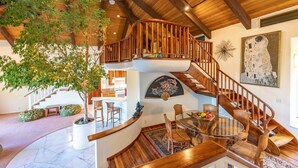 Un interior espacioso con una escalera de madera, un comedor y un gran árbol.