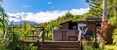 A wooden deck with steps leading to a building, surrounded by lush greenery and a clear blue sky.