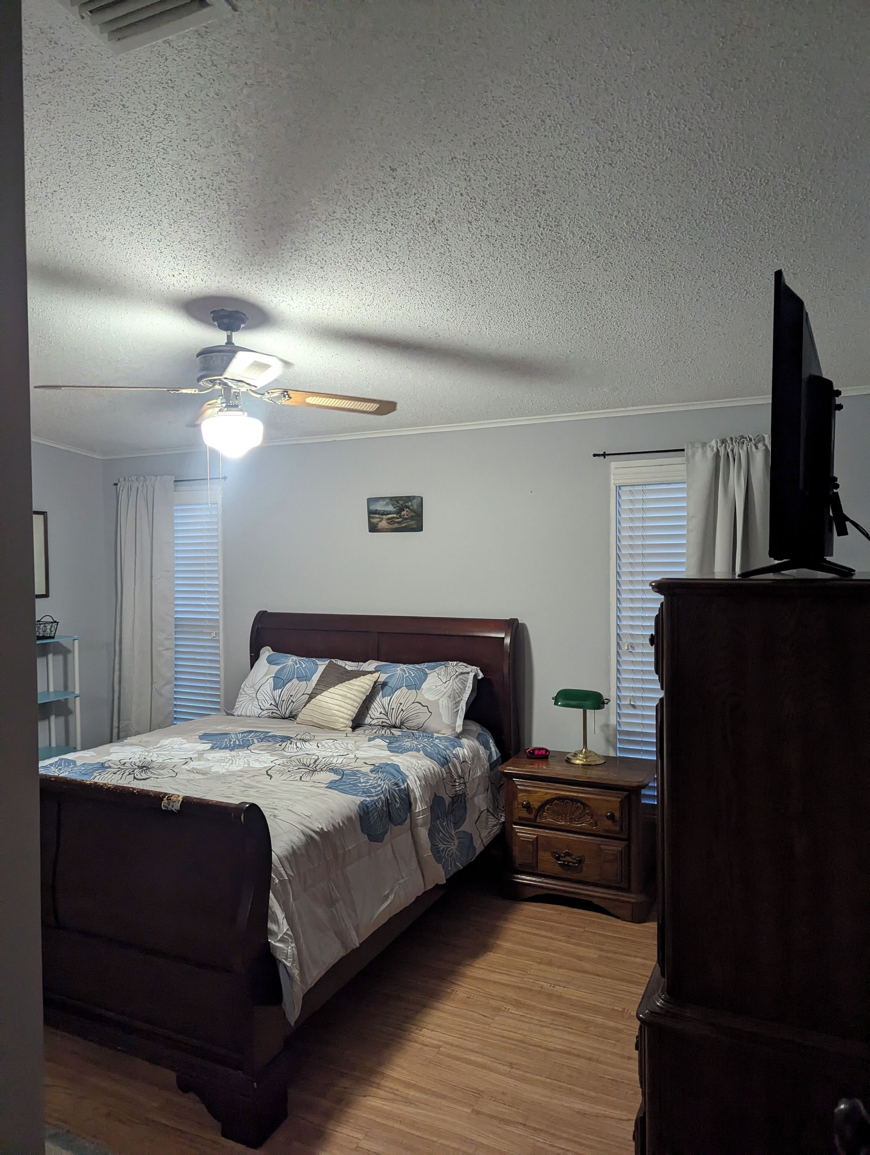 A bedroom with a bed, nightstand, dresser, ceiling fan, and a picture on the wall.