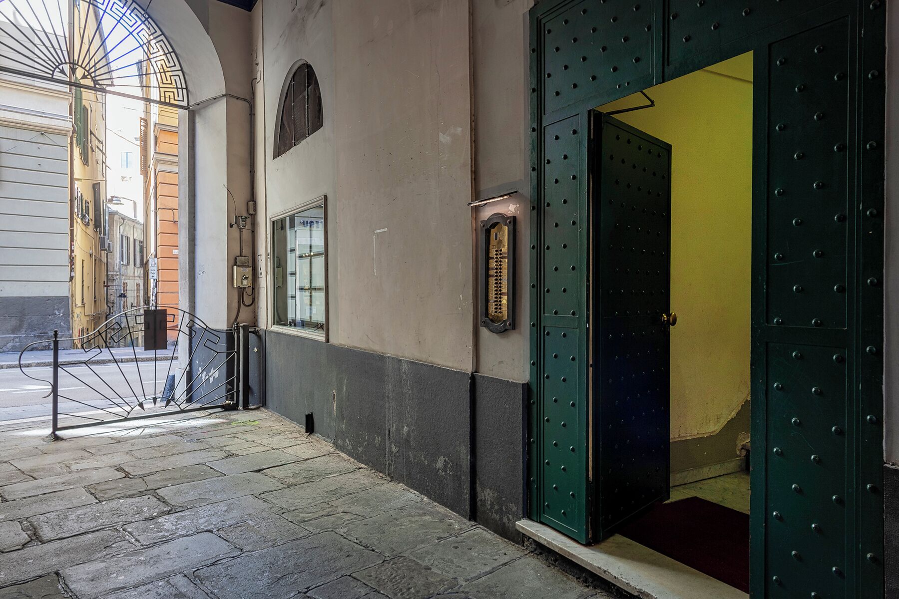 A narrow alleyway with a metal gate, a small window, and a door with a security lock.