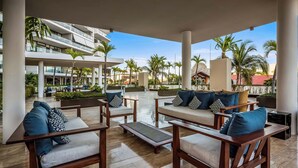A rooftop lounge with outdoor seating, palm trees, and a view of a hotel building. - Luxury Waterfront 2BR Condo w/ Pool, Gym & Bar, Puerto Vallarta (Puerto Vallarta)