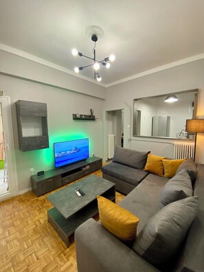 Een moderne woonkamer met een grijze bank, een flatscreen televisie, een salontafel en een plafondlamp.