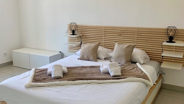 A modern bedroom with a wooden bed frame, white bedding, and two bedside tables with decorative lamps. - Cozy 3-bedroom apartment with WiFi, AC in amazing Bonifacio (Bonifacio)