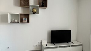 A modern living room with a flat-screen TV on a white stand, a globe, and framed photos on shelves. - Cozy 3-bedroom apartment with WiFi, AC in amazing Bonifacio (Bonifacio)