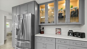 Cocina moderna con gabinetes grises, refrigerador de acero inoxidable y una encimera con cafetera y tostadora.