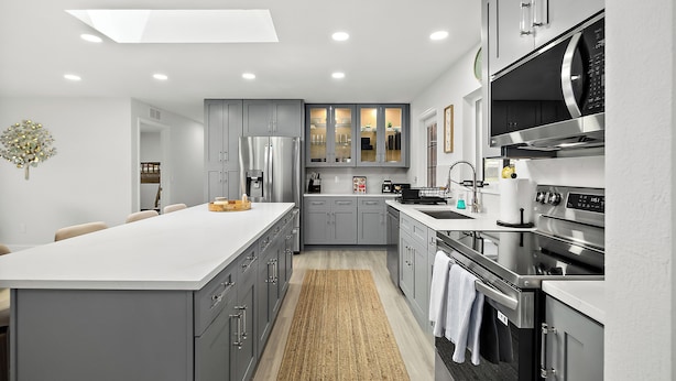 Una cocina moderna con armarios grises, una isla central y electrodomésticos de acero inoxidable.