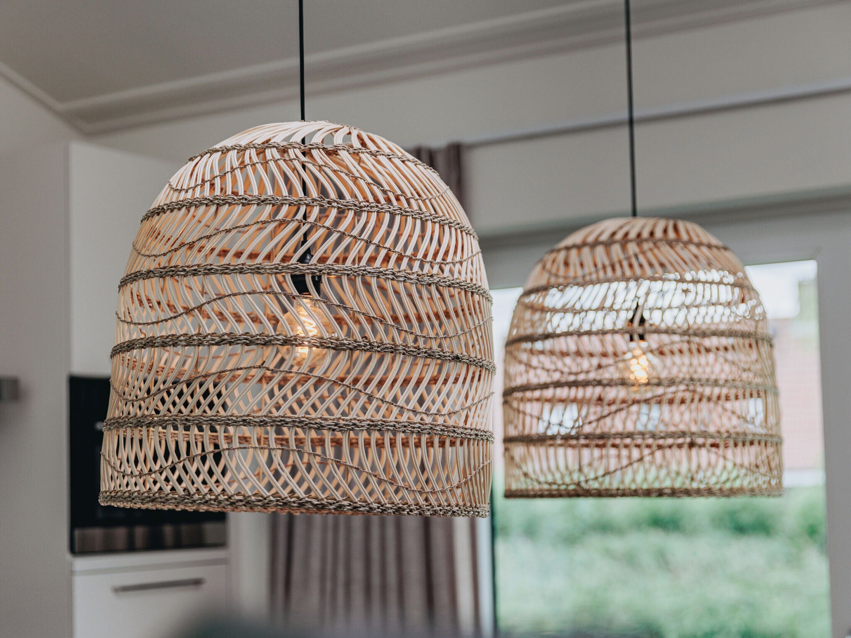 Zwei gewebte Pendelleuchten hängen von der Decke in einer modernen Küche mit Blick auf Grünflächen.
