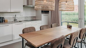 Una cocina moderna con armarios blancos, un lavamanos de acero inoxidable y una zona de comedor con mesa y sillas de madera.