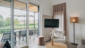 Un salón moderno con televisor, una mesa redonda de centro, un sofá y un amplio ventanal con vistas a una terraza.