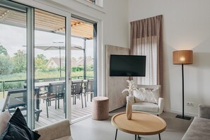 A modern living room with a TV, a round coffee table, a sofa, and a large window overlooking a deck. - Modern Lodge Near Beach (Breskens)