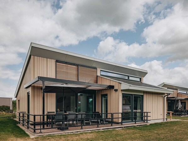 A modern building with a flat roof, large windows, and a covered outdoor seating area with tables and chairs. - Modern Lodge Near Beach (Breskens)