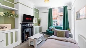 Ein modernes Hotelzimmer mit Fernseher, einem grünen Sofa, einem Bett, einem Kamin und einem fenster mit Vorhängen.