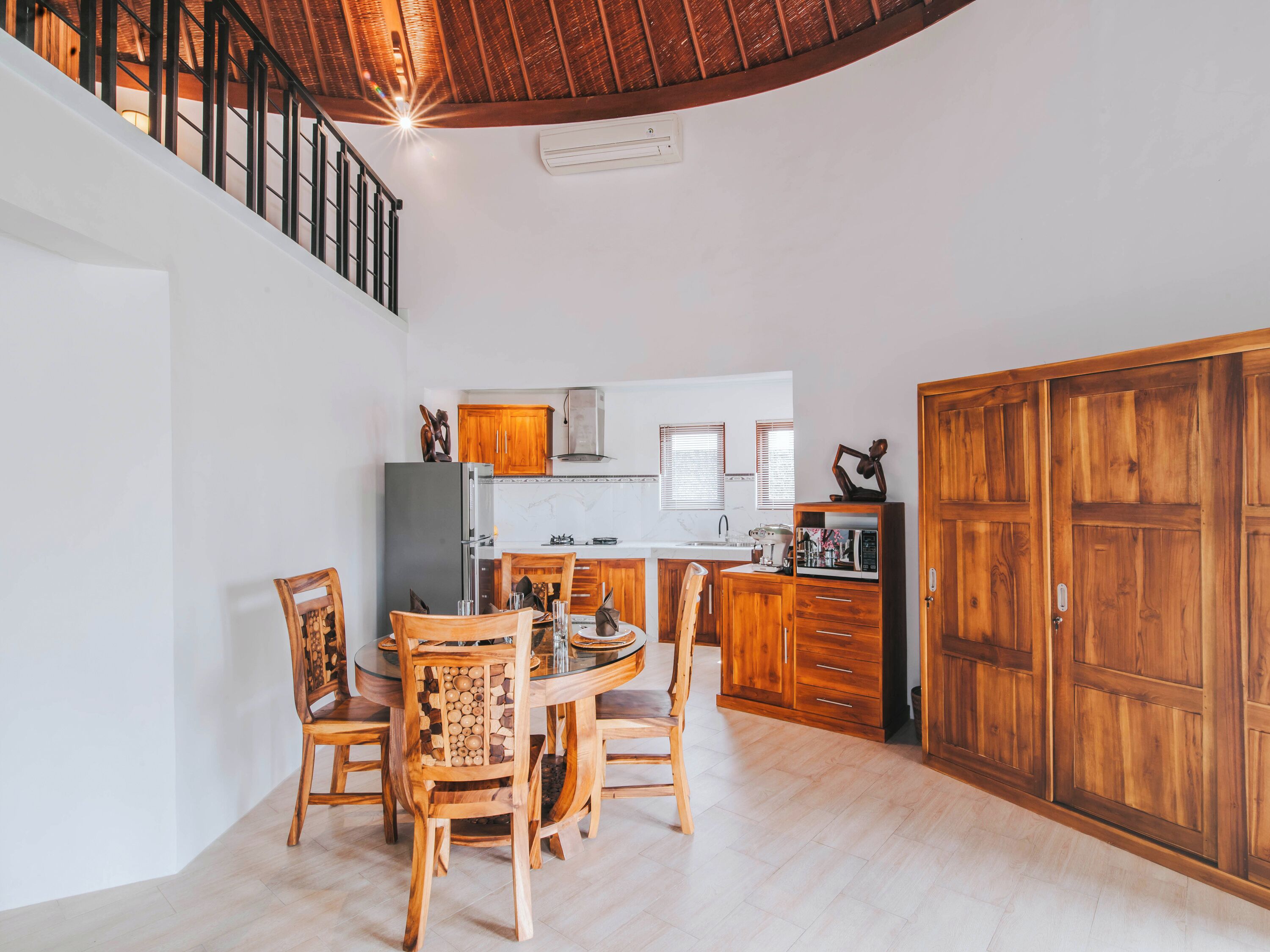 Un coin repas avec une table ronde et des chaises en bois, une cuisine avec des meubles en bois et une grande armoire en bois.