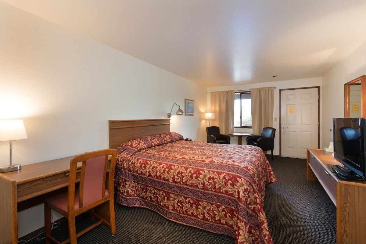A hotel room with a bed, desk, chair, TV, and a small table.