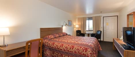 A hotel room with a bed, desk, chair, TV, and a small table.