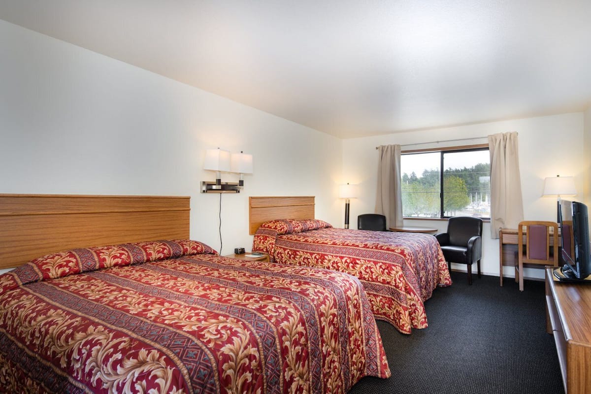 A hotel room with two beds, a desk with a chair, a television, and a window with a view.