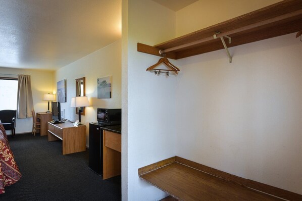 A hotel room with a bed, desk, chair, TV, and a wooden shelf. - Cap Sante Inn (Anacortes)