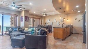 A spacious living area with a large sofa, ottoman, and a dining area with a high ceiling fan.