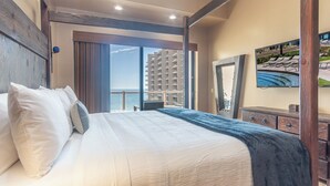A hotel room with a large bed, a view of the sea, and a balcony with a pool.