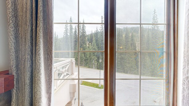 A room with a large window overlooking a forested area. - Hearthstone Lodge #327 (Sun Peaks)