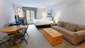 A hotel room with a bed, a sofa, a wooden chest, a desk with a chair, and a television. - Hearthstone Lodge #327 (Sun Peaks)