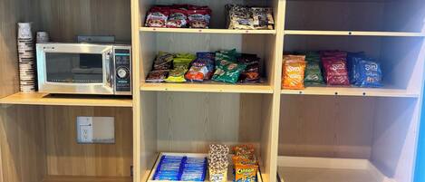 A kitchenette with a microwave, various snack packets, and a drawer with blue items.