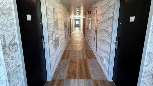 A hallway with patterned walls and wooden flooring, leading to multiple doors. - Hotel Rudra - Hollywood (Los Angeles)