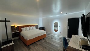 A modern hotel room with a large bed, bedside tables, a desk with a chair, a TV, and a mirror on the wall. - Hotel Rudra - Hollywood (Los Angeles)