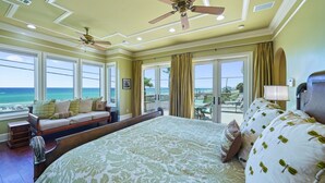 Ein geräumiges Schlafzimmer mit einem großen Bett, einem Deckenventilator und Blick auf den Ozean durch große Fenster.