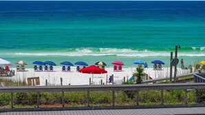 Ein Strand mit Reihen von Liegestühlen und Sonnenschirmen, einer Holzpromenade und einem Schild, das privaten Zugang zum Strand kennzeichnet.