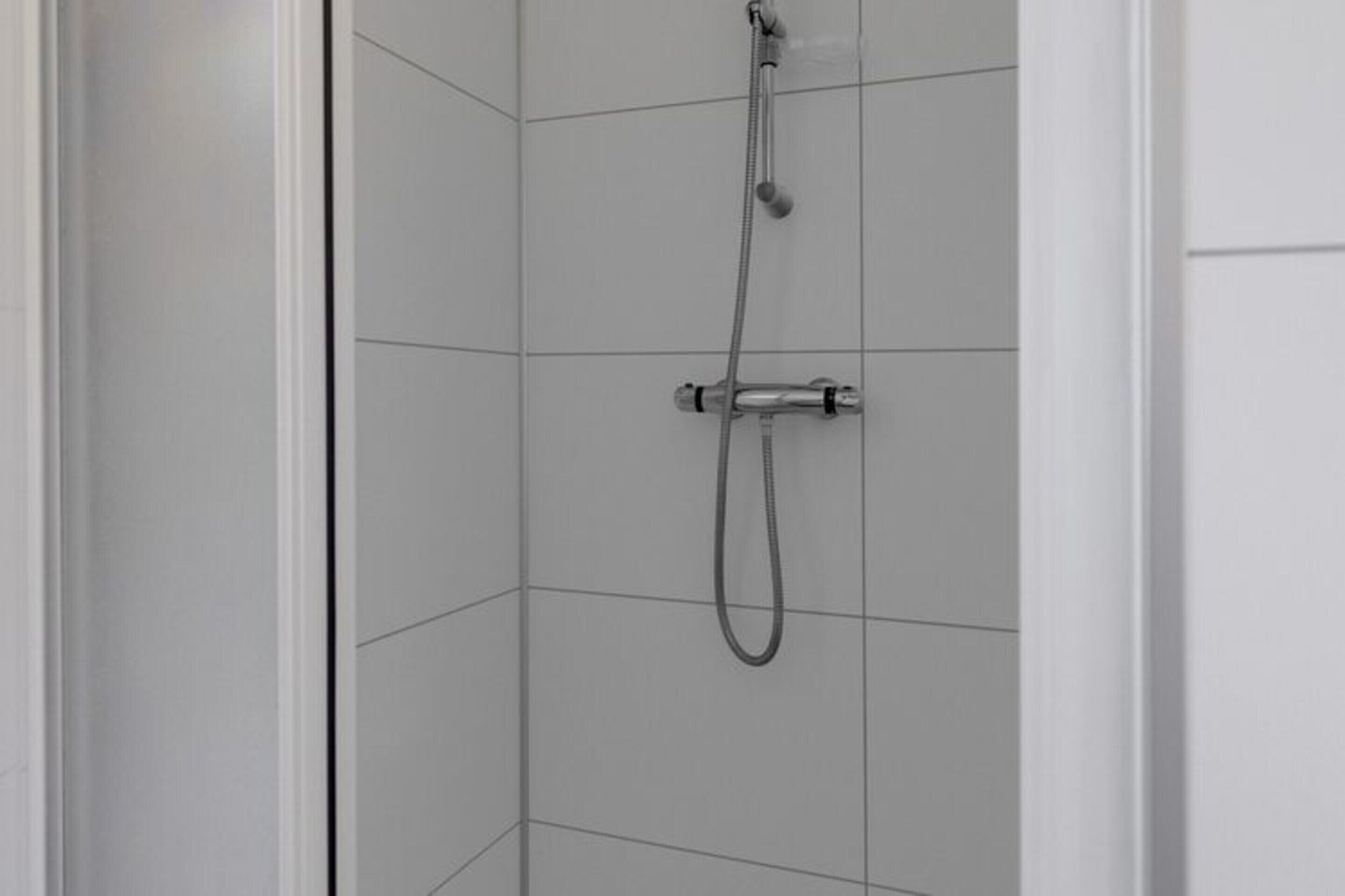 Une douche équipée d’un pommeau de douche à main et d’un robinet mural dans une salle de bain carrelée.