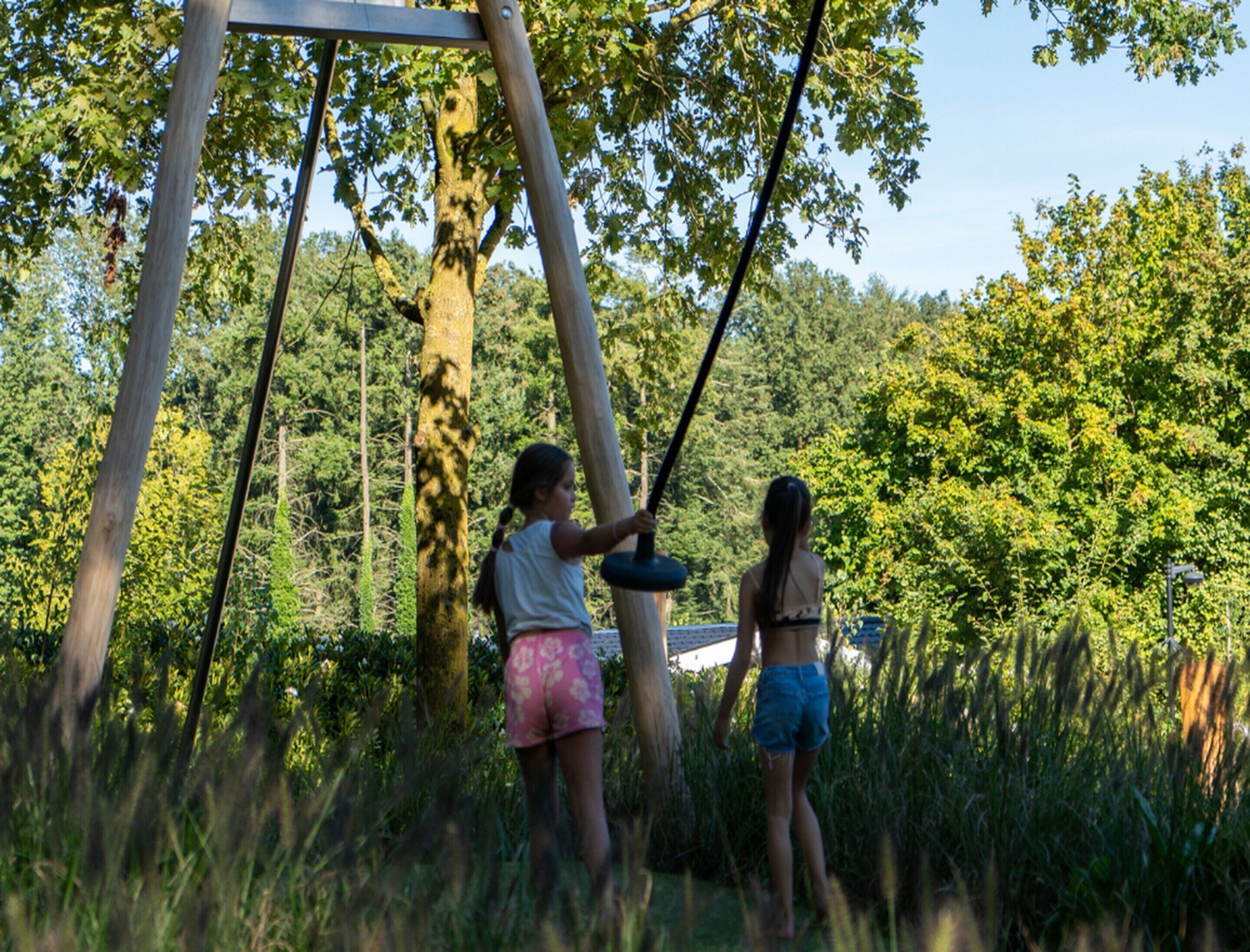 Dos personas se balancean en un columpio en un área boscosa.