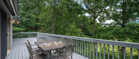 Une terrasse en bois avec une table et des chaises, entourée d’arbres et offrant une vue sur un paysage verdoyant.