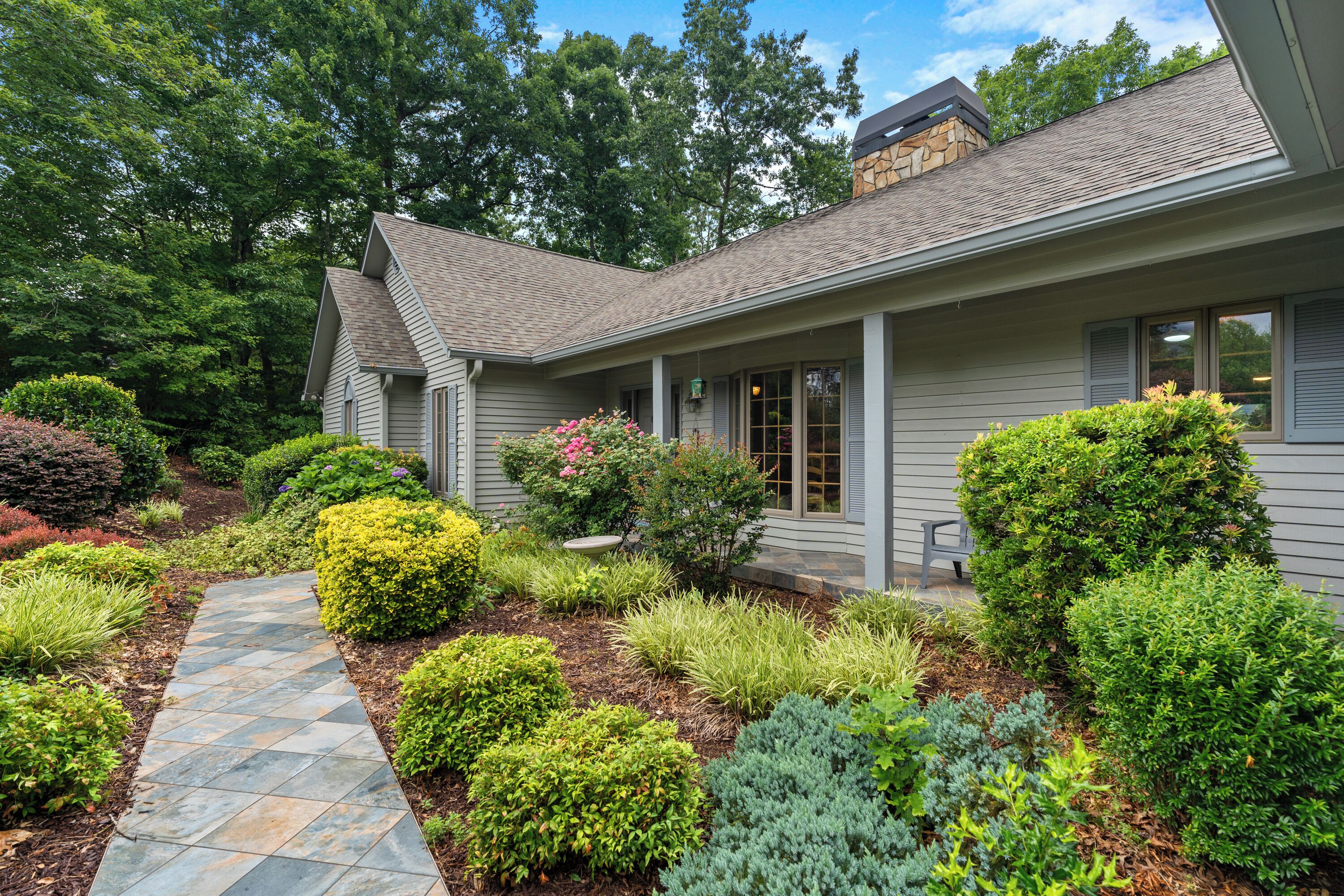 A house with a stone pathway leading to the entrance, surrounded by various shrubs and plants.