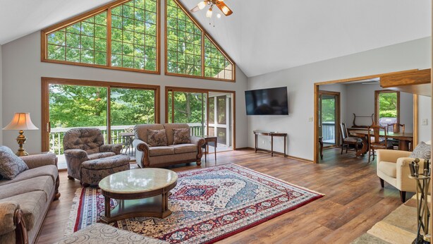 A spacious living room with large windows, a ceiling fan, and a flat-screen TV.