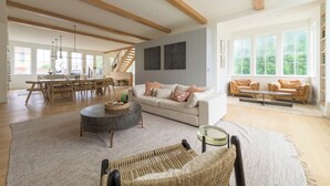 A spacious living area with a high ceiling, a dining area, and large windows providing natural light.