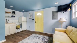 A compact kitchen with white cabinets, a yellow door, and a beige sofa. - Tiny House 20 Mins from Beach (Brunswick)