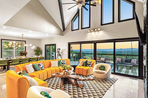 A spacious living room with a large sofa set, a coffee table, and a view of the outdoors through large windows.