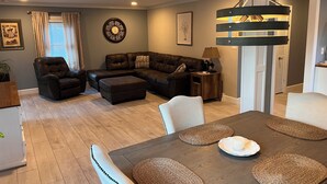 A modern living room with a sectional sofa, a dining table with placemats, and a chandelier. - The Cardinals Nest, Charming 4-bedroom house, Historic Village of Ballston Spa.  (Ballston Spa)