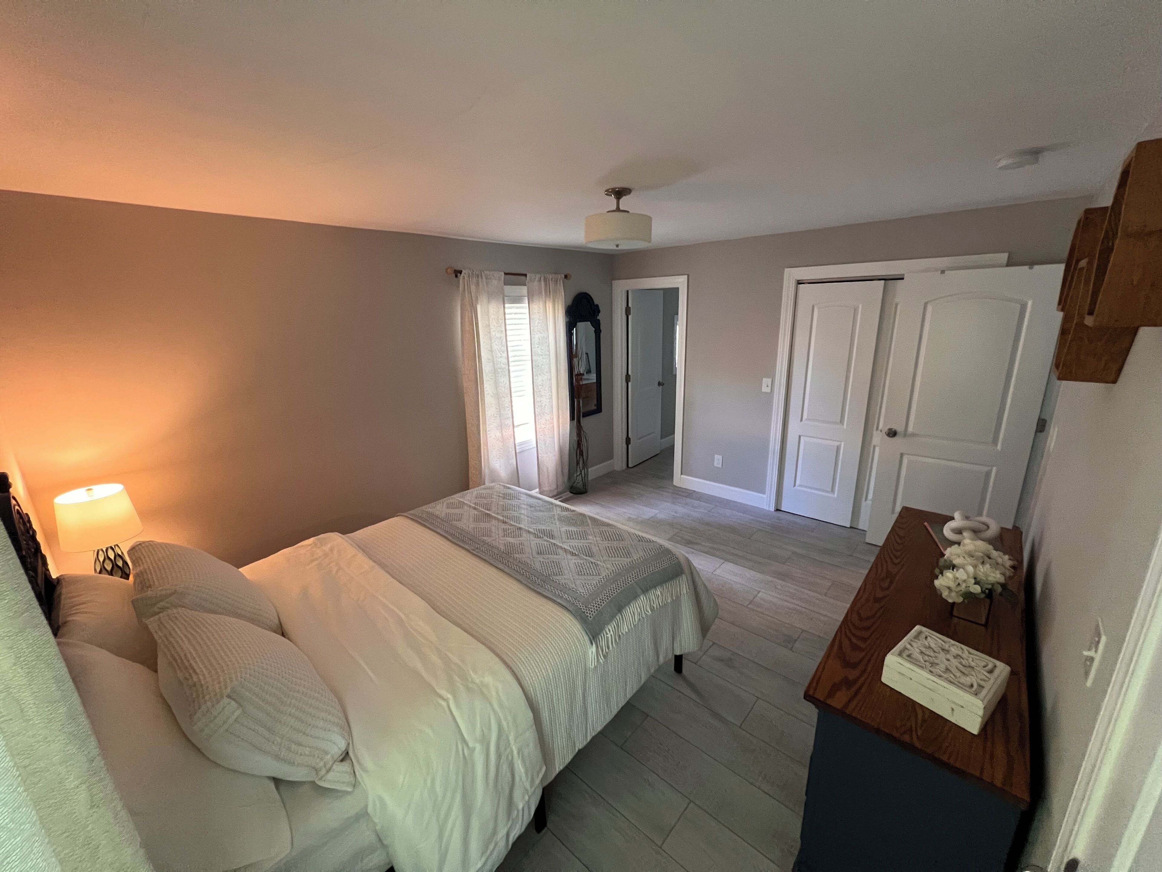 A bedroom with a bed, a nightstand, a lamp, a dresser, and a door.