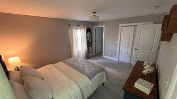 A bedroom with a bed, a nightstand, a lamp, a dresser, and a door.