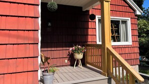 A red wooden house with a porch, a hanging spherical decoration, and a window with a white frame. - The Cardinals Nest, Charming 4-bedroom house, Historic Village of Ballston Spa.  (Ballston Spa)