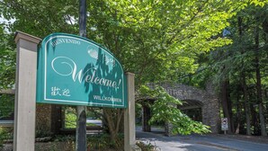 A welcome sign with multilingual greetings, set against a backdrop of lush greenery and a stone structure. - Beary Cozy | Pets, Work Station & 20 Min. from AVL (Black Mountain)
